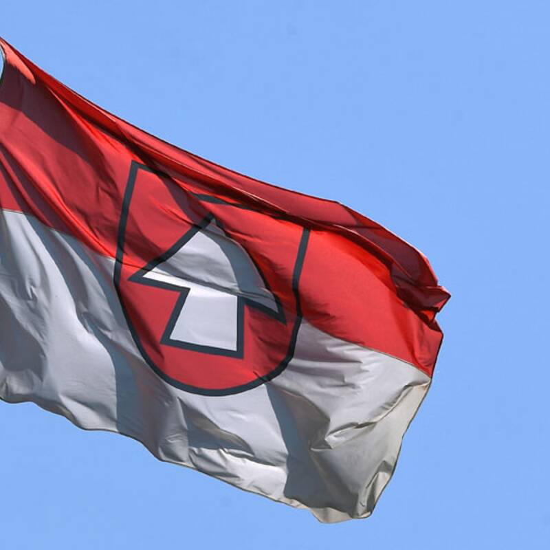 Eine Flagge mit einem roten und weißen Muster weht vor einem klaren blauen Himmel.
