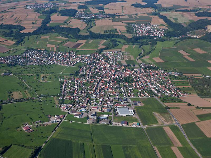 Luftaufnahme einer ländlichen Gegend mit einem Dorf in der Mitte, umgeben von grünen Feldern und Wäldern.