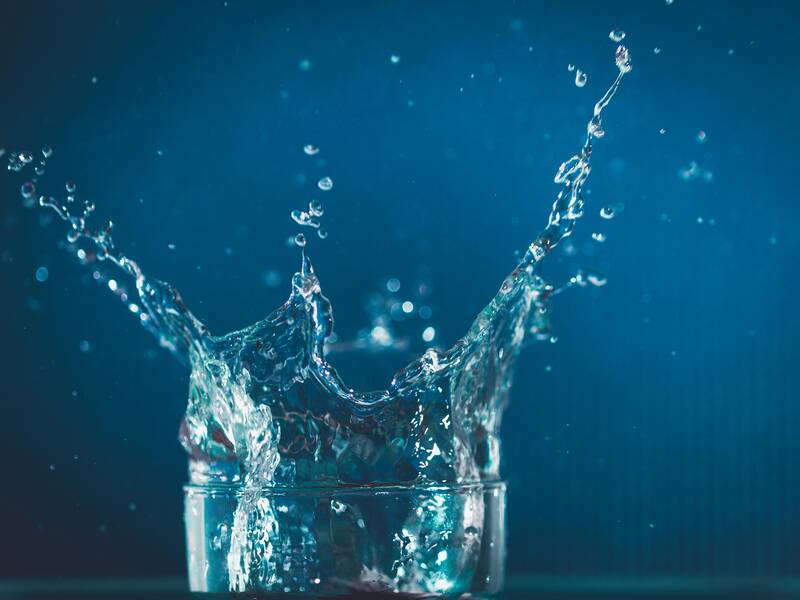 Ein Wassertropfen fällt in ein Glas und erzeugt eine große, spritzende Krone aus Wasser.