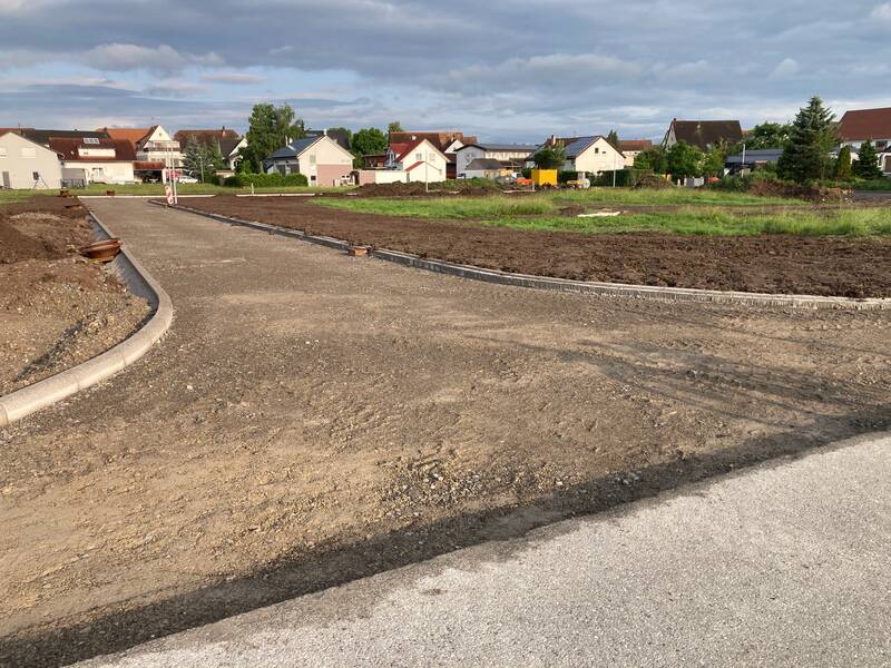 Eine Brachfläche mit einer unbefestigten Straße im Vordergrund wird von einer Reihe von Wohnhäusern im Hintergrund begrenzt.