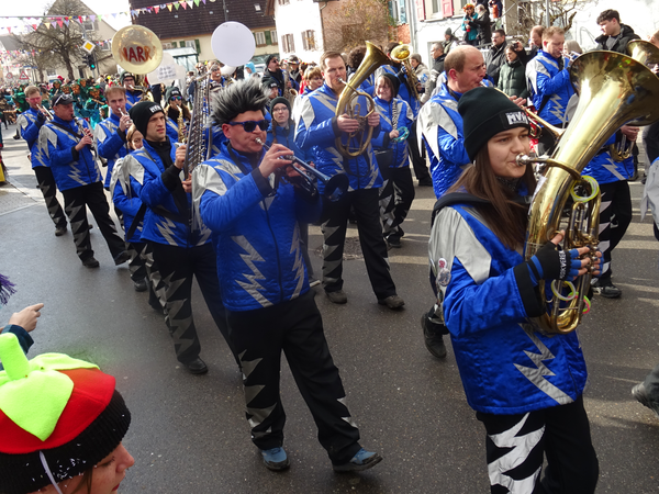 Eine Gruppe von Musikern in blauen und schwarzen Kostümen mit Instrumenten marschiert bei einem Straßenumzug.