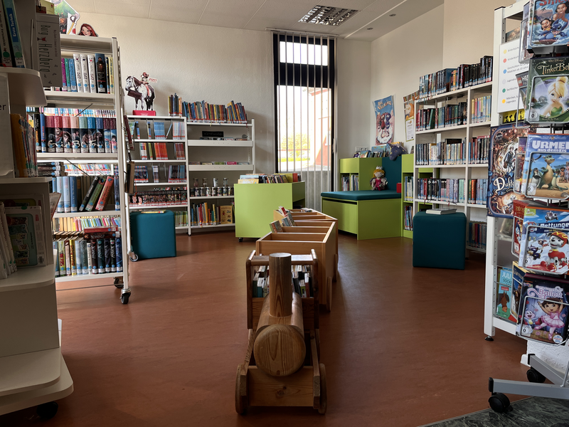 Ein einladender Kinderbereich in einer Bibliothek mit Regalen voller Bücher, einem Holzspielzeugzug im Vordergrund und bunten Sitzgelegenheiten.