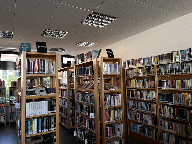 Ein Raum mit mehreren Bücherregalen voller Bücher und verschiedenen thematischen Beschriftungen.