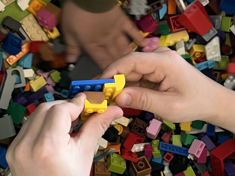 Einige Kinderhände greifen in eine grüne Kiste voller bunter Lego-Steine.