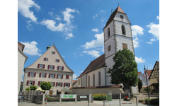 Eine historische Kirche mit einem hohen Glockenturm und angrenzendem Eis-Café vor einem blauen Himmel mit einigen Wolken.