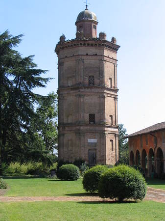 Ein hoher, dreistöckiger Ziegelturm mit einer Kuppel steht in einer grünen, gepflegten Landschaft neben einem Gebäudeflügel mit Arkaden.
