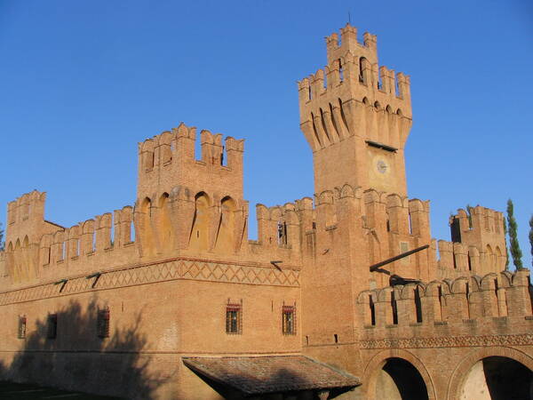 Ein altes, aus roten Ziegeln gebautes Schloss mit hohen Türmen und Zinnen steht vor einem klaren blauen Himmel.