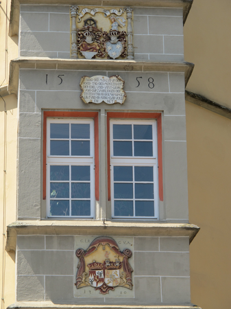 An einer Gebäudeaußenwand sind zwei verzierte Wappen und eine Inschrift zwischen den Fenstern aus dem Jahr 1558 zu sehen.
